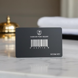 Peut inclure: Une carte de chambre rectangulaire noir mat avec un emblème de palmier blanc dans un bouclier, le texte HARBOUR POINT RESORT, un code-barres vertical avec les chiffres 0 492713 8 en dessous et les mots ROOM KEY dans le coin inférieur droit.