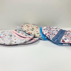 Könnte beinhalten: Vier Topflappen mit Blumenmustern. Die Topflappen sind aus Stoff und haben eine hellblaue, rosa und weiße Farbgebung.