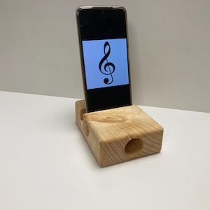 Könnte beinhalten: Ein Holz-Telefonständer mit einem Loch vorne, um den Klang zu verstärken. Ein Smartphone ist in den Ständer gestellt und zeigt einen Violinschlüssel auf dem Bildschirm.