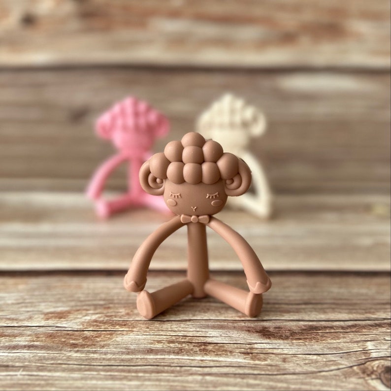 May include: A brown silicone baby teether shaped like a sheep with a bow tie. The teether has a textured surface and is designed for babies to chew on.