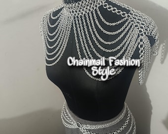 May include: Silver chainmail necklace and belt set. The necklace is a choker style with multiple chains hanging down the front. The belt is a wide band with multiple chains hanging down the front. The set is made of silver chainmail.
