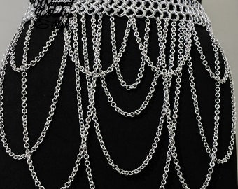 May include: A silver chainmail belt with a long chain fringe hanging from the bottom. The belt is made of small, interconnected metal rings.