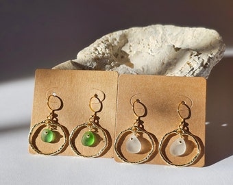 May include: Two pairs of gold hoop earrings with a textured finish. One pair features a green sea glass charm, and the other pair features a white sea glass charm.