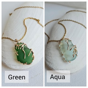 K&ouml;nnte beinhalten: Zwei Halsketten mit goldenen Ketten und Anh&auml;nger aus Meerglas. Das Meerglas ist in ein goldenes Drahtdesign eingefasst. Das Meerglas links ist gr&uuml;n und das Meerglas rechts ist aquafarben.