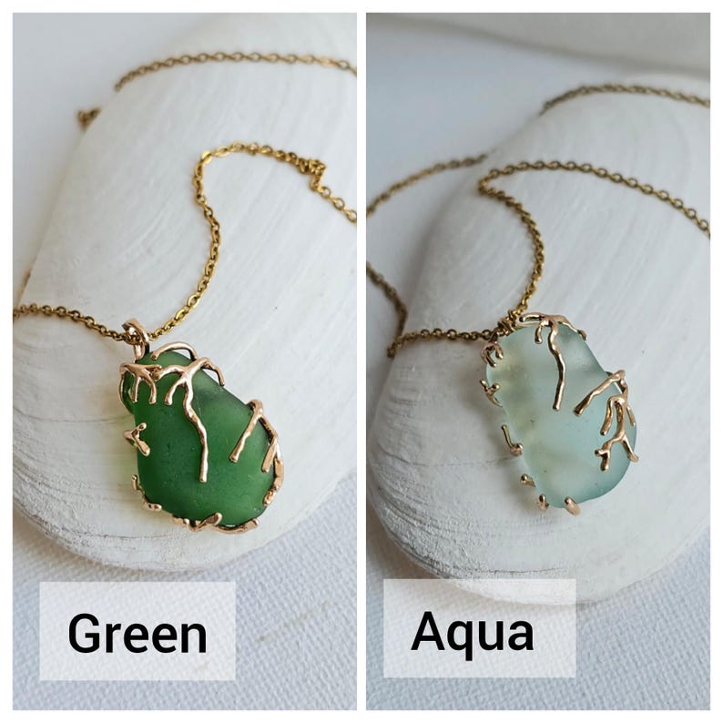 K&ouml;nnte beinhalten: Zwei Halsketten mit goldenen Ketten und Anh&auml;nger aus Meerglas. Das Meerglas ist in ein goldenes Drahtdesign eingefasst. Das Meerglas links ist gr&uuml;n und das Meerglas rechts ist aquafarben.