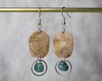 May include: A pair of silver earrings with oval-shaped wooden pendants and green stone accents. The wooden pendants have a natural wood grain pattern.