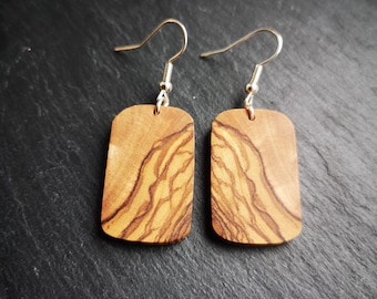 May include: A pair of olive wood earrings with a natural wood grain pattern. The earrings are rectangular in shape and have silver hooks.