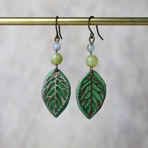 Könnte beinhalten: Ein Paar grüne Blatt-Ohrringe mit einem filigranen Drahtdesign. Die Ohrringe sind mit hellgrünen und weißen Perlen verziert.