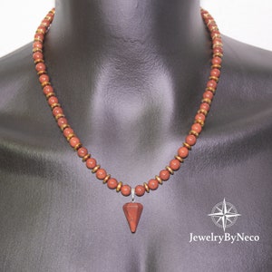 May include: A necklace featuring reddish-brown beads and gold-colored spacers. A triangular, reddish-brown pendant hangs from the center. The necklace is displayed on a black mannequin. The JewelryByNeco logo is visible in the lower right corner.