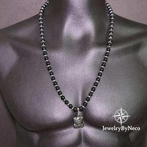 May include: A black beaded necklace with a silver turtle pendant. The necklace has small, round black beads separated by silver spacers. The turtle pendant has a textured shell design. The necklace is displayed on a black mannequin.