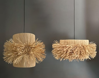 May include: Two hanging light fixtures with natural woven shades. The shades are made of a light brown material that resembles straw or natural fibers. The shades have a fringe-like texture around the edges.