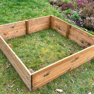 May include: A rectangular raised garden bed made from natural brown wood planks. The bed is sitting on a grassy lawn.