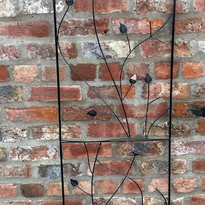 May include: Black metal garden trellis featuring a decorative design of leaves and branches. The trellis is arched at the top and is built to last.