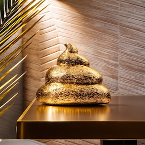 May include: A gold-colored ceramic sculpture of a pile of poop. The sculpture is sitting on a gold-colored table.