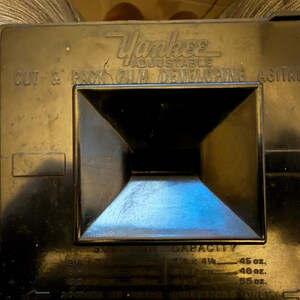 May include: Black Yankee Adjustable Cut & Pack Film Developing Agitank. The top of the tank has the brand name and product information. The tank has a square, recessed center. The tank has capacity measurements in ounces.