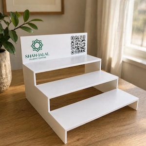Könnte beinhalten: Ein weißer, dreistufiger Präsentationsständer mit dem Text "SHAH-JALAL ISLAMIC CENTRE" und einem grünen geometrischen Logo. Ein QR-Code ist auf der obersten Ebene aufgedruckt. Der Ständer ist für die Präsentation von Artikeln konzipiert.