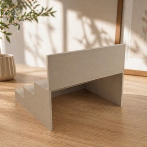 May include: A light beige, three-step display stand with a back panel. The stand is made of a solid material and is positioned on a wooden surface. The design is minimalist and modern, suitable for showcasing small items.