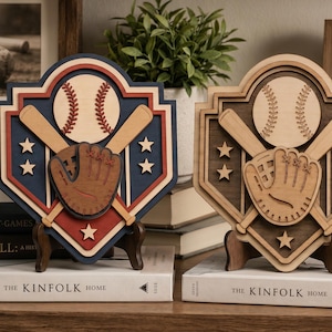 May include: Two layered wooden baseball plaques on stands. The left plaque features a blue, red, and cream color scheme with a baseball, crossed bats, a glove, and stars. The right plaque is monochromatic in shades of brown and cream with identical motifs.
