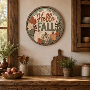 May include: A circular wooden wall sign featuring the text Hello FALL in raised lettering. The design includes three pumpkins, one with a leopard print pattern, surrounded by autumn leaves and berries in shades of orange, green, and cream.