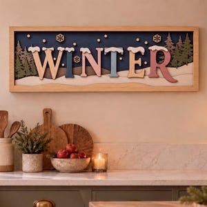 May include: A rectangular wooden wall sign featuring the word WINTER in multi-colored, layered 3D letters. The design includes a dark blue background with silhouettes of green pine trees, white snow-capped peaks, and small wooden snowflake accents.