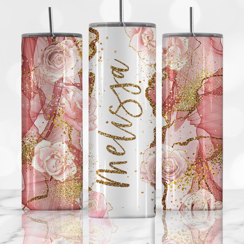 K&ouml;nnte beinhalten: Drei Edelstahlbecher mit einem rosa-goldenen Blumendesign. Der mittlere Becher tr&auml;gt den Namen "Melissa" in goldenen Glitzer.
