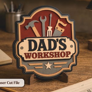 May include: A multi-layered wooden sign with the text "DAD'S WORKSHOP" and tool silhouettes. The sign features a red background with a black and gray border, and a star and stripes design. The sign is displayed on a wooden stand.