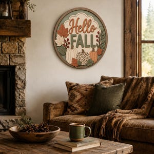 May include: A circular wooden wall sign featuring the text Hello FALL in raised lettering. The design includes layered cutouts of three pumpkins, one with a leopard print pattern, surrounded by various autumn leaves and berries in muted tones.