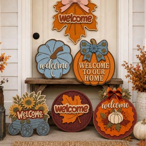 May include: A collection of six decorative wooden signs featuring seasonal motifs including pumpkins, sunflowers, and maple leaves. Each sign displays the word welcome or welcome to our home in various fonts, colors, and layered designs.