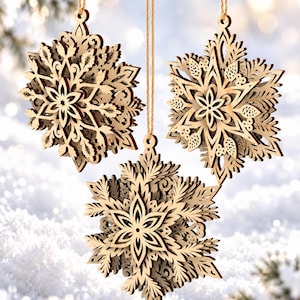 May include: Three laser-cut wooden snowflake ornaments with intricate, layered geometric patterns. Each ornament features a light brown natural wood finish and is suspended by a thin, light-colored twine string for hanging.
