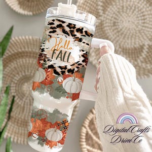 Op de afbeelding: Een witte tumbler met een luipaardprint, herfstbladeren en pompoenen. De tumbler heeft een rietje en een handvat. De tekst "Hello Fall" staat op de tumbler.