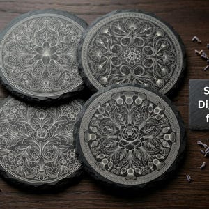 May include: Four round black slate coasters with intricate white floral and geometric designs. The coasters are arranged on a dark wooden surface, with a small square slate tile that reads "SVG Digital file".