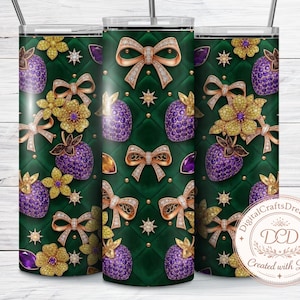 Puede incluir: Un vaso verde con un patrón repetido de lazos dorados, fresas moradas con incrustaciones de joyas y flores doradas. El diseño está sobre un fondo acolchado con detalles dorados. El vaso incluye una pajita plateada.