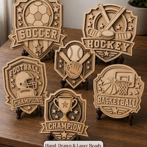 May include: A collection of six layered wooden sports plaques featuring engraved designs for soccer, hockey, football, baseball, basketball, and a champion trophy. Each shield-shaped sign includes stars and text labels. A label reads Hand-Drawn & Laser Ready.