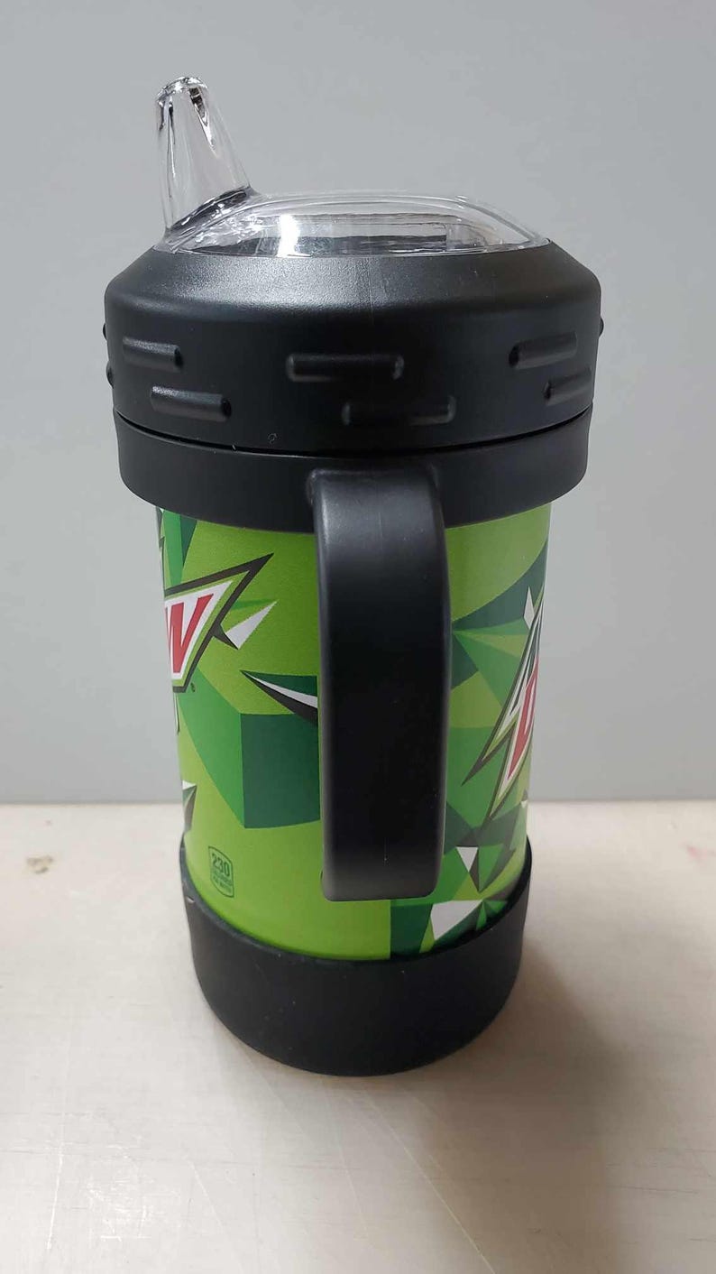 May include: Green and black insulated travel mug with a black handle and a clear lid with a spout. The mug has a Mountain Dew logo and a geometric pattern.