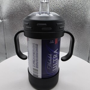 Pode incluir: Uma caneca preta com bico com al&ccedil;as, um bico transparente e uma tampa preta. A caneca foi projetada para conter uma lata de cerveja Michelob Ultra. A lata &eacute; vis&iacute;vel atrav&eacute;s da caneca e apresenta uma marca azul e branca.