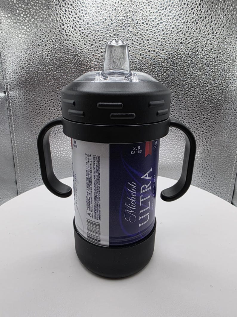 Pode incluir: Uma caneca preta com bico com al&ccedil;as, um bico transparente e uma tampa preta. A caneca foi projetada para conter uma lata de cerveja Michelob Ultra. A lata &eacute; vis&iacute;vel atrav&eacute;s da caneca e apresenta uma marca azul e branca.