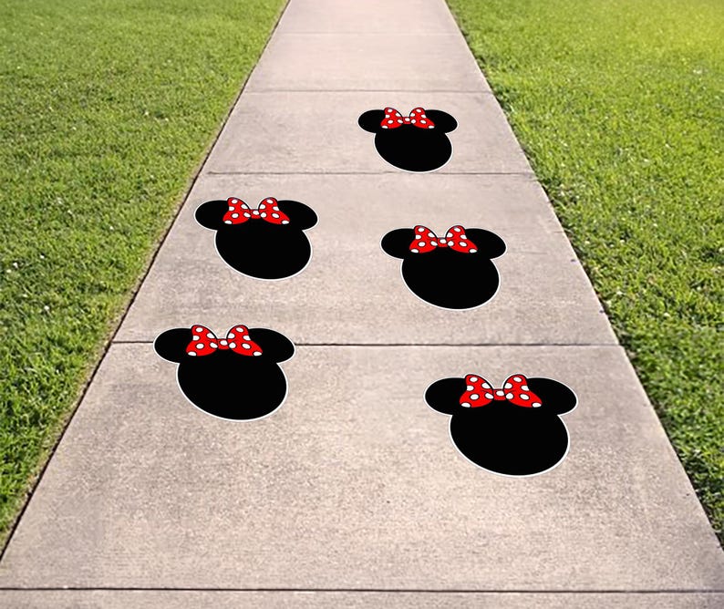 May include: Five black Minnie Mouse head-shaped decals with red and white polka dot bows are arranged on a concrete sidewalk. The decals are spaced apart, creating a playful and whimsical design on the walkway.