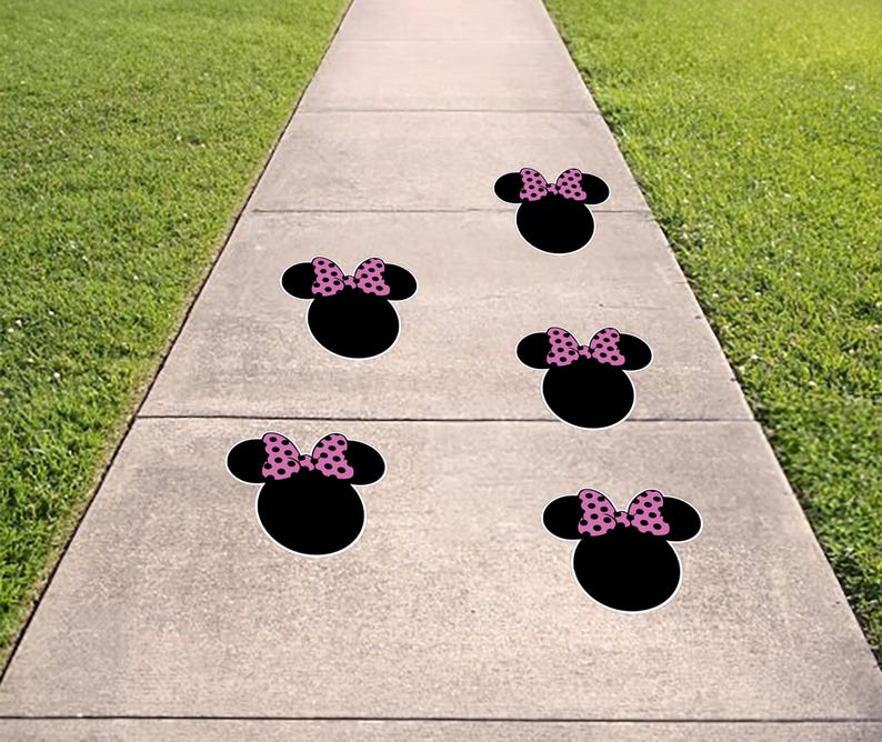 May include: Five black Minnie Mouse head-shaped sidewalk decals with pink polka dot bows are arranged on a concrete walkway. The decals are spaced apart, leading the eye down the path.