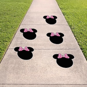 Puede incluir: Calcoman&iacute;as negras con forma de cabeza de rat&oacute;n con lazos rosas de lunares. Las calcoman&iacute;as est&aacute;n colocadas en una acera de hormig&oacute;n, con hierba verde a ambos lados.