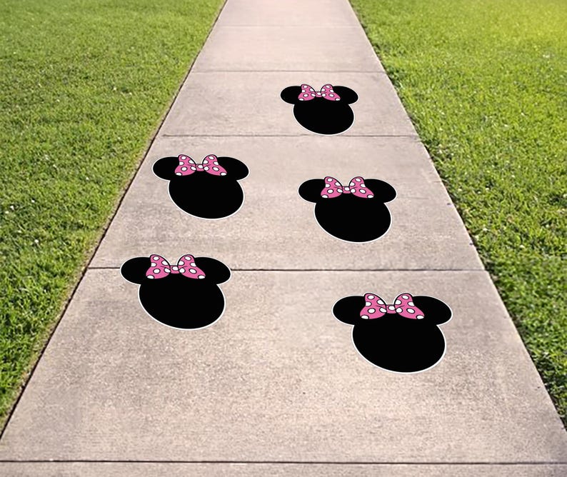 Puede incluir: Calcoman&iacute;as negras con forma de cabeza de rat&oacute;n con lazos rosas de lunares. Las calcoman&iacute;as est&aacute;n colocadas en una acera de hormig&oacute;n, con hierba verde a ambos lados.