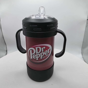 May include: A red and black sippy cup featuring the Dr. Pepper logo. The cup has a clear, plastic top with a spout, two black handles, and a black base. The Dr. Pepper logo is white with a red outline and the words "Est. 1885".