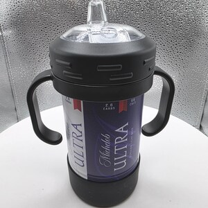 Pode incluir: Uma caneca preta com duas al&ccedil;as, uma parte superior transparente e uma base preta. A caneca &eacute; embrulhada com um r&oacute;tulo de lata de cerveja Michelob Ultra. O r&oacute;tulo &eacute; azul e branco com as palavras "ULTRA" e "Michelob Ultra".