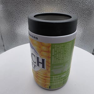 Puede incluir: Un enfriador de latas cil&iacute;ndrico con una tapa negra y un dise&ntilde;o con mazorcas de ma&iacute;z. El texto "Ranch" es visible en la parte delantera. El enfriador tiene una banda blanca con la palabra "FARMERS" impresa.