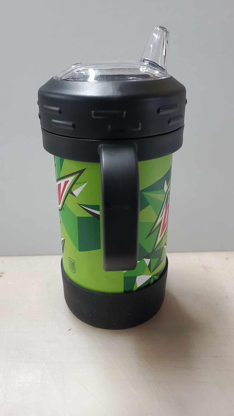 May include: Green and black travel mug with a black handle and a clear lid with a spout. The mug has a Mountain Dew logo and a geometric pattern.