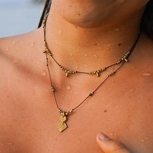 Può includere: Due collane d'oro con piccole perline e un ciondolo d'oro a forma di spirale. Le collane sono sul petto di una persona.