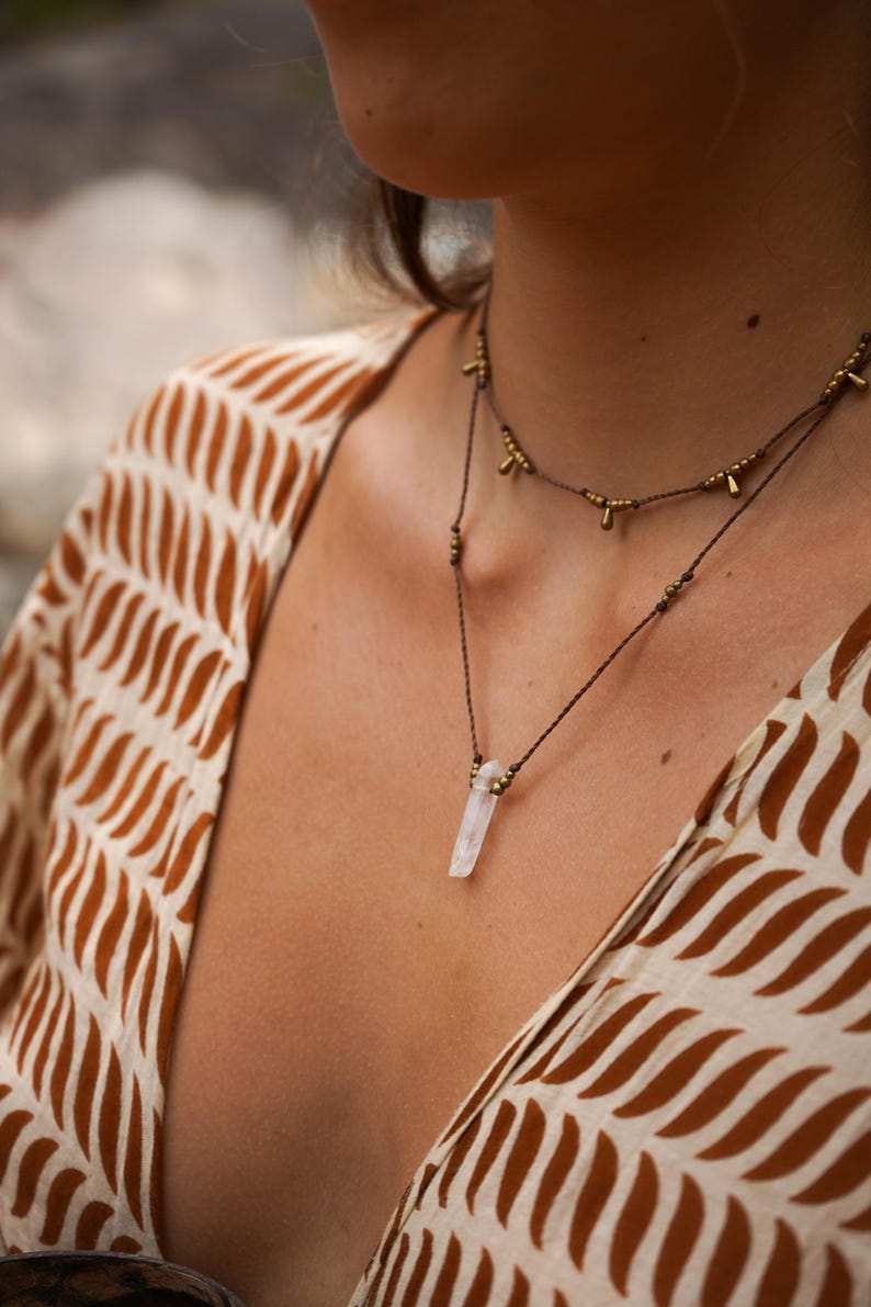 May include: A delicate necklace with a clear quartz crystal pendant and gold accents. The necklace is made with brown cord and small gold beads.