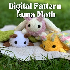 Peut inclure: Trois animaux en peluche crochetés en forme de papillons de nuit luna. Les papillons de nuit sont de différentes couleurs, notamment le vert, le blanc, le rose et le jaune. Les papillons de nuit sont assis sur une serviette blanche sur un lit d'herbe verte.
