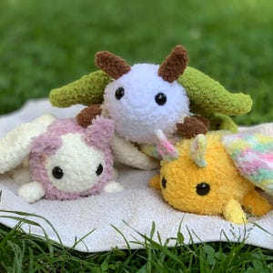 May include: Three crocheted stuffed animals, a white one with green wings, a pink one with white wings, and a yellow one with pink and green wings.