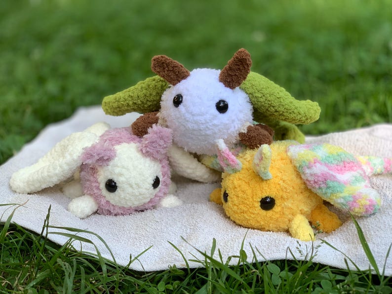 May include: Three crocheted stuffed animals, a white one with green wings, a pink one with white wings, and a yellow one with pink and green wings.