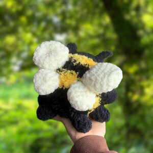 May include: A crocheted bumble bee plush toy with black and yellow stripes and white fuzzy wings.